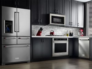 A kitchen wall featuring dark cabinets and KitchenAid stainless steel refrigerator, microwave, stove and dishwasher appliances.