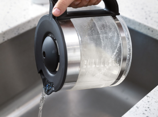 A coffee maker with vinegar and baking soda being emptied into a sink, emphasizing affresh® coffee maker cleaner’s effectiveness.