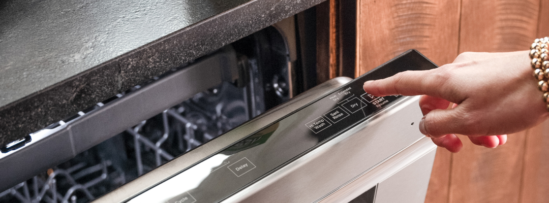 Person pressing the sanitize cycle button on a stainless steel dishwasher, demonstrating how to deep clean a dishwasher using the sanitize setting.